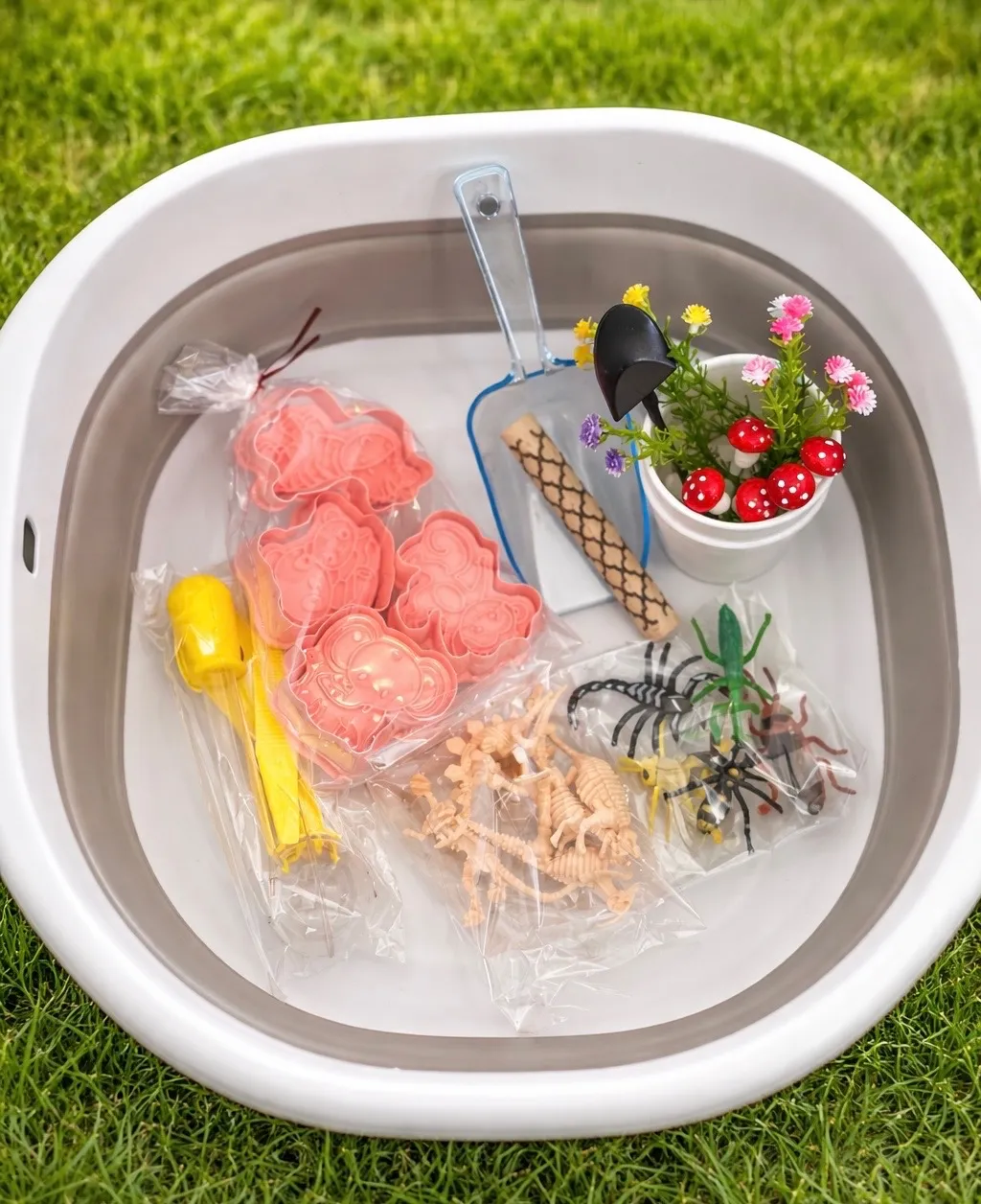 Collapsible sensory play bucket with toy insects, dinosaur figures, scoops, stamps, mushrooms, and flowers